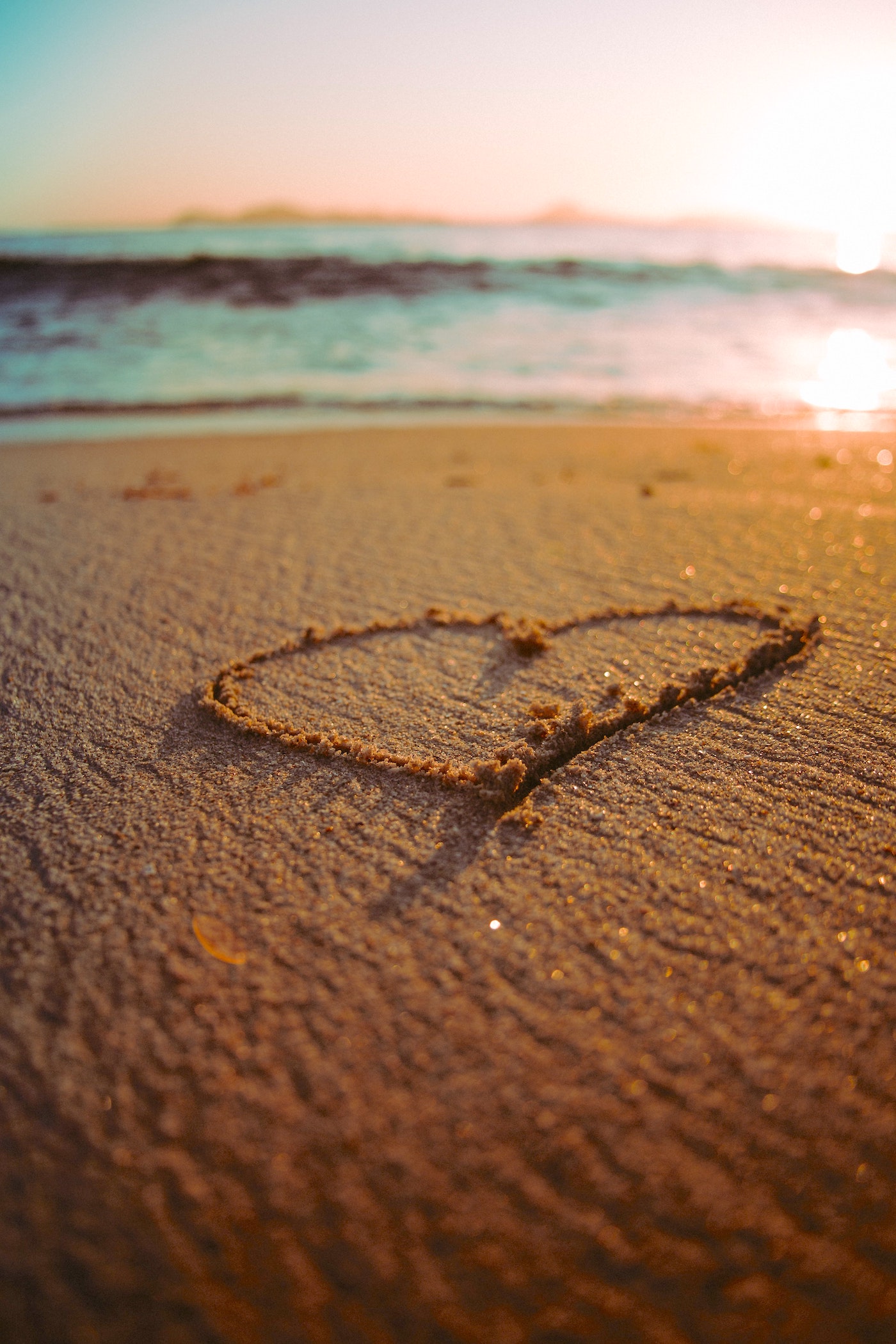A heart shape drawn in the sand on a beach at sunset