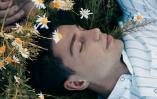 A person lying peacefully among daisies and wildflowers with eyes closed