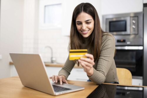 young woman smiling while holding credit card to put in laptop to pay for service