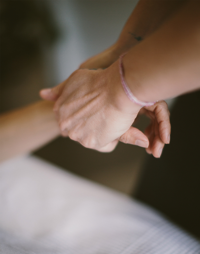 A gentle hand resting near another person's wrist, evoking therapeutic touch