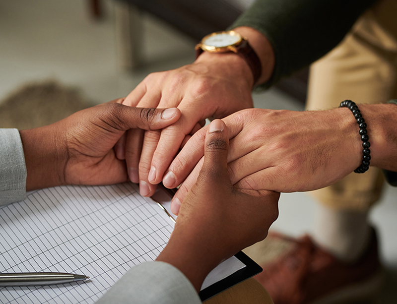 Hands clasped in support Two people's hands clasped together over a desk, a gesture of connection and support during a session