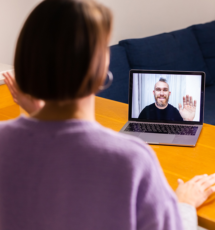 Online video session A woman on a video call waving to a man on her laptop screen, evoking an online therapy session