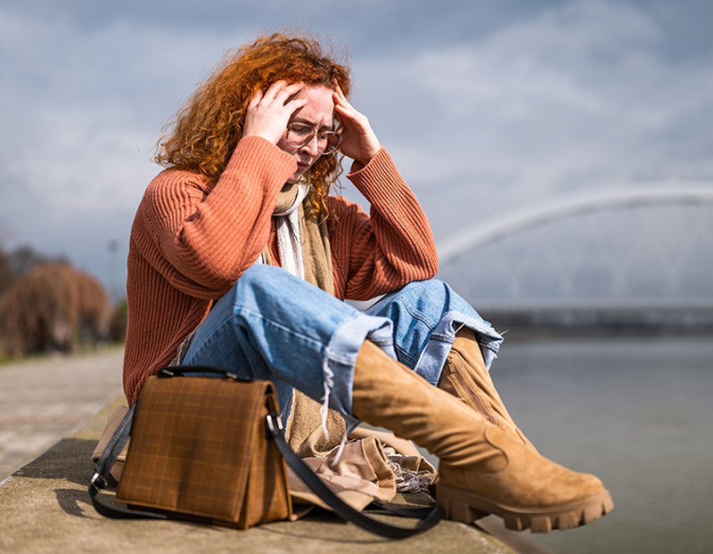 Woman overwhelmed by anxiety A woman sitting on the ground with her hand to her head looking overwhelmed, evoking anxiety, trauma, and depression