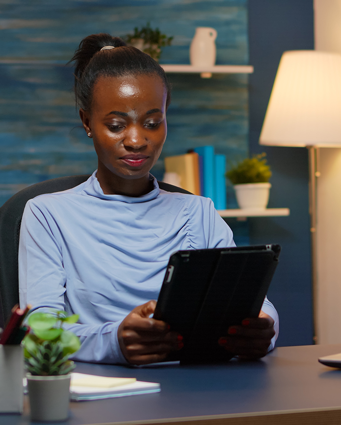 Woman reading a tablet at home A woman at a desk in the evening reading a tablet, evoking online or telehealth engagement