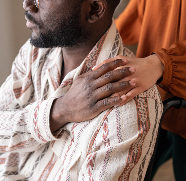 A hand resting gently on a man's chest from behind, evoking comfort and therapeutic touch