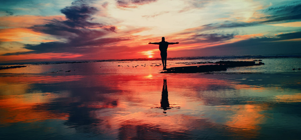 Arms open to the sunset A person standing on a reflective beach at sunset with arms wide open, evoking freedom and release