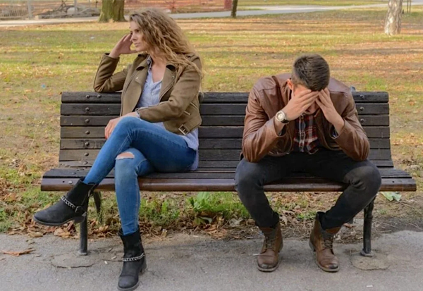 couple on bench looking away young couple on bend in park. she looking away body angled away, him looking down head in hands