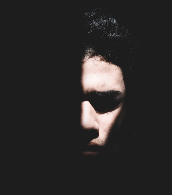 Face half in shadow A young man's face half emerging from deep shadow, evoking heaviness, depression, and inner darkness