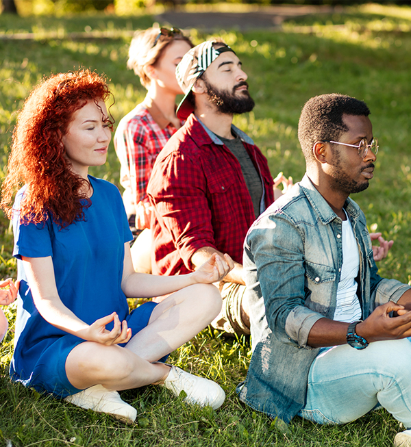 A diverse group sitting cross-legged meditating together outdoors on the grass, evoking community and shared practice