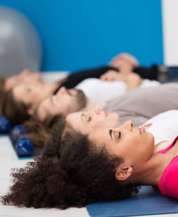 Several people lying on mats with eyes closed during a group relaxation, breathwork, or meditation session