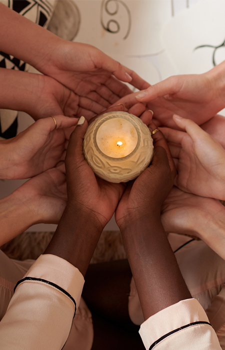 Hands holding a candle in ritual Several people's cupped hands holding a lit candle together, evoking ritual, ceremony, and community