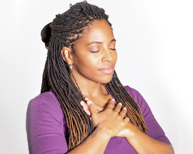 Hands over heart, self-compassion A woman resting both hands over her heart with eyes closed, a gesture of self-compassion and embodiment