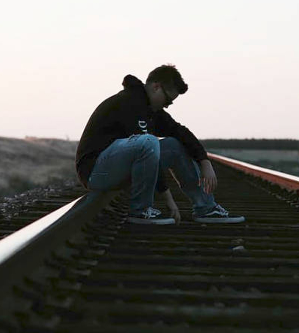 Man alone on railroad tracks A young man sitting hunched on railroad tracks looking alone and isolated, evoking despair