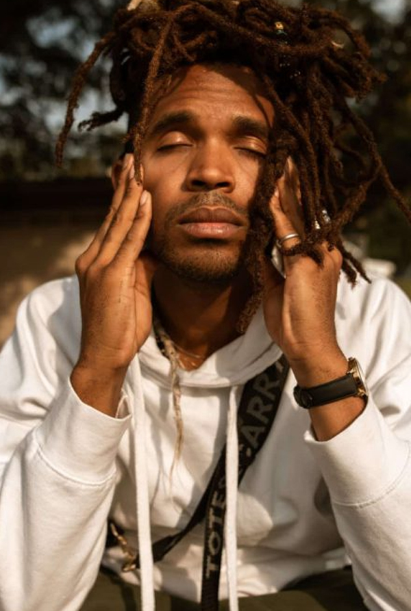 Man in inward focus A man with locs and eyes closed, hands resting on his cheekbones, turned inward in reflection