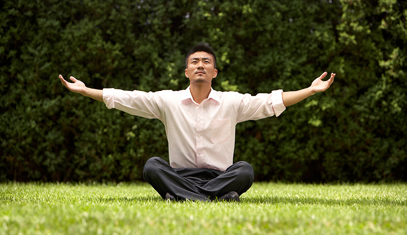 Man meditating with open arms A man sitting cross-legged on the grass with arms open wide in a gesture of openness and gratitude