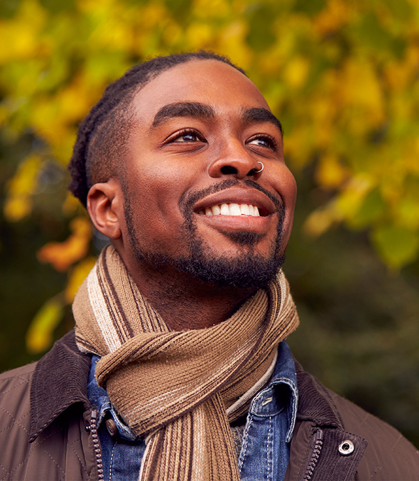 Man smiling outdoors in autumn A man in a scarf looking upward with a hopeful smile amid autumn foliage
