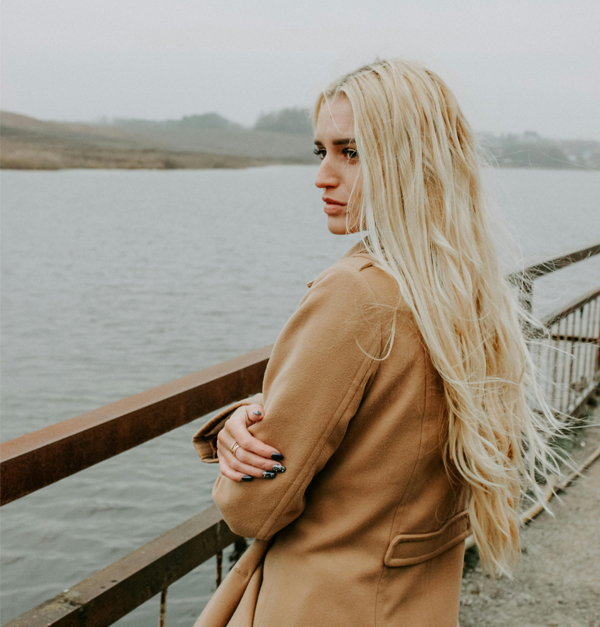 Pensive woman by the water A woman with long blonde hair holding her own arms on a pier by the water, looking thoughtful