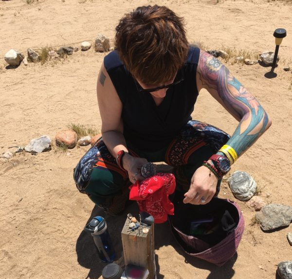 Ritual in the desert – Sabrina Santa Clara Sabrina Santa Clara kneeling on desert ground arranging objects in a ceremony, evoking neoshamanic ritual and rites of passage