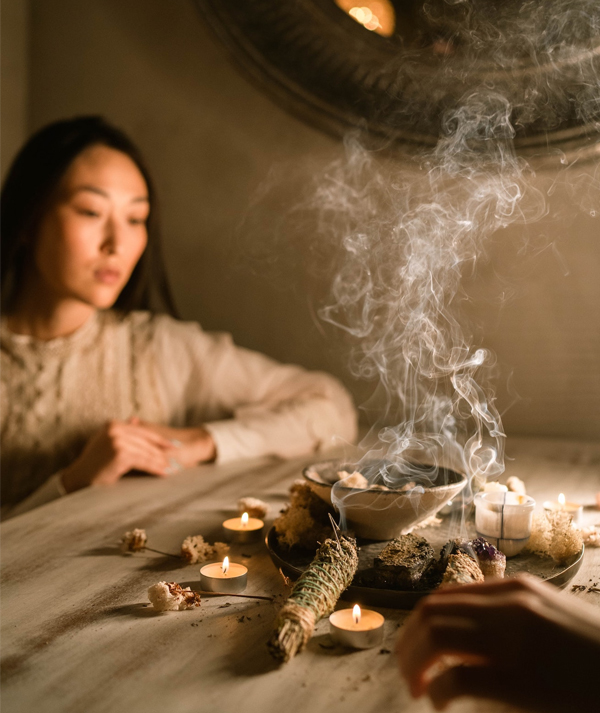 Smudging with sage A woman burning sage at a table with smoke rising, evoking a cleansing smudging ritual