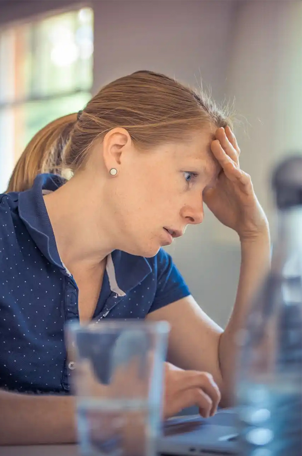 Woman dissociating at her desk A woman at a desk with her hand to her forehead, looking dazed or dissociated