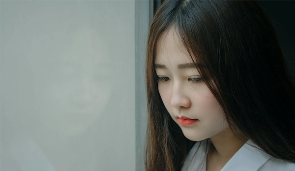 Woman looking down, sad A young woman leaning against a wall looking down, evoking sadness and loneliness