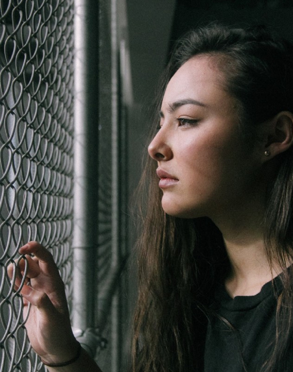 Woman looking through a fence A woman holding a chain-link fence and gazing through it with a sad expression, evoking longing and isolation