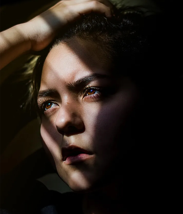 Woman with a worried expression A young woman in dramatic light and shadow with a furrowed, worried brow, evoking anxiety