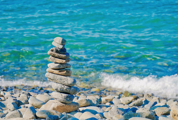 A balanced stack of stones forming a cairn on a rocky ocean shore, evoking balance and intention