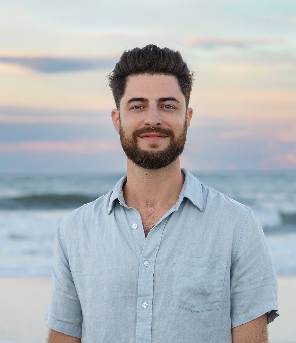 Portrait of Matt Colaciello in a blue shirt on the beach, inviting holistic coaching