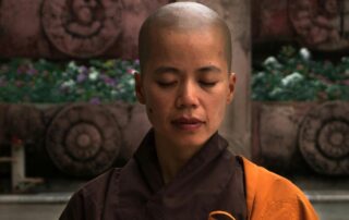 bald buddhist nun taking refuge in meditation in zen courtyard