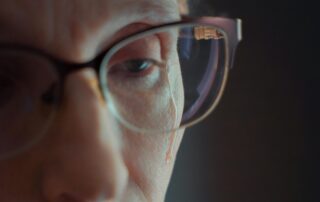 Close-up of an older woman in glasses looking down in grief
