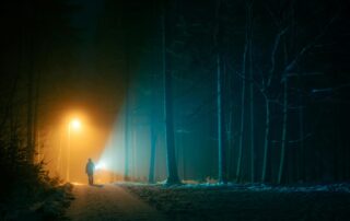 person under light in dark forest