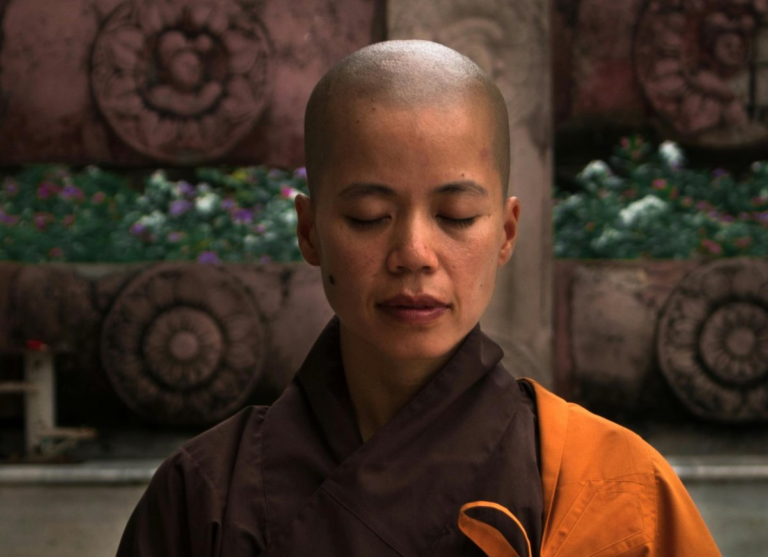 A bald Buddhist nun sits in meditation in a sunlit Zen courtyard, taking refuge in practice.