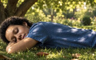 Woman resting face down on the grass beneath a tree in dappled afternoon light