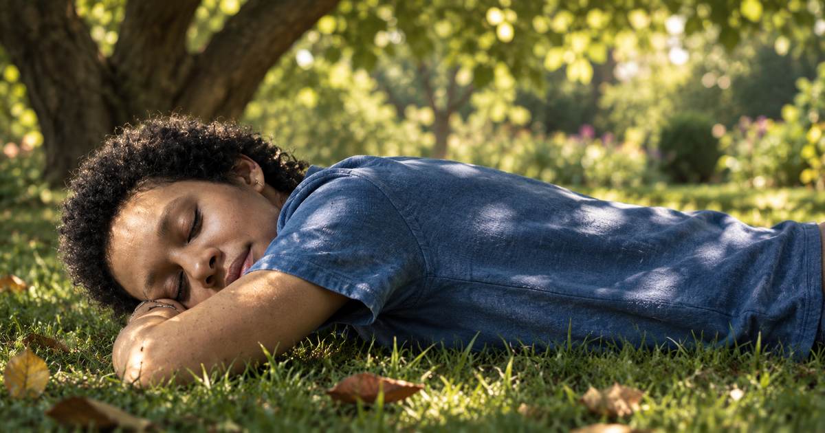 Woman resting face down on the grass beneath a tree in dappled afternoon light