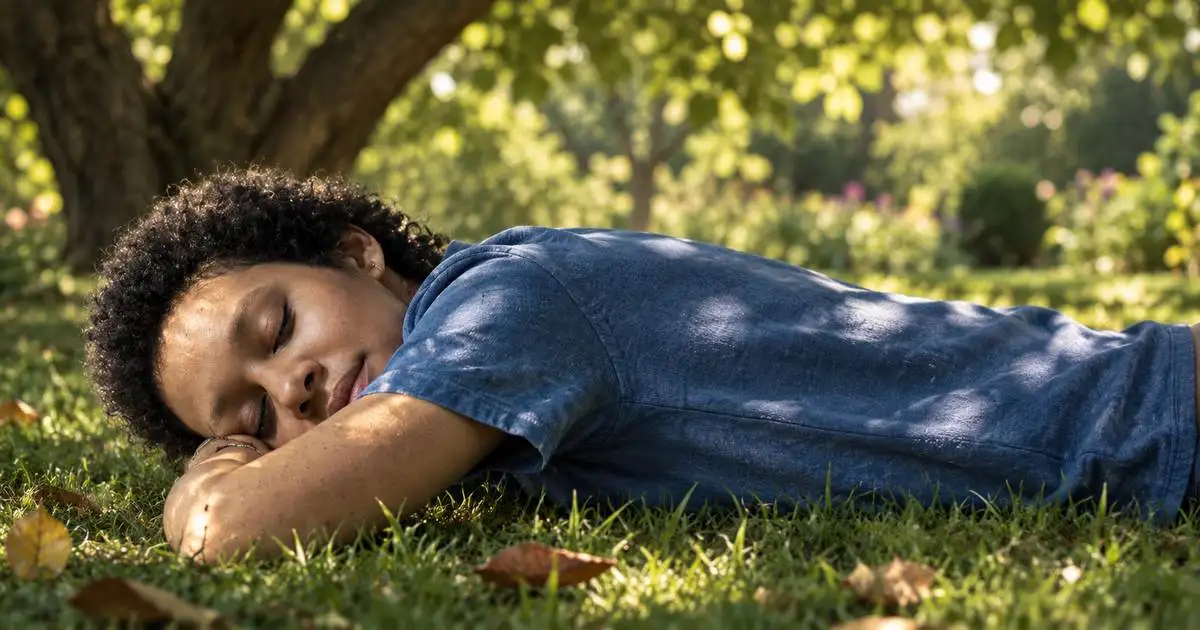 Woman resting face down on the grass beneath a tree in dappled afternoon light
